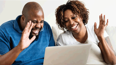 Man & woman on a video call smiling and waving at laptop screen.